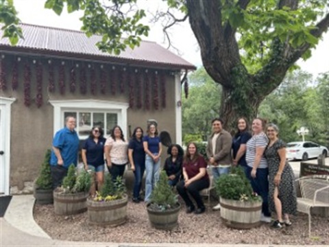 The Finance Division Staff is standing in front of Rancho de Chimayo in the afternoon