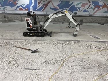 Picuture of mid-size machinary to grind out plaster and tile. Machinary is sitting in an empty olympic pool, and a blue and red mural painted in the background.