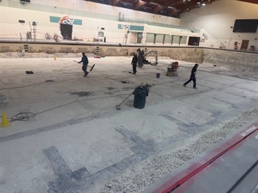 An empty olympic size pool, with workers working to remove old plaster.