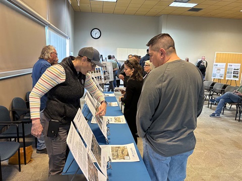 Project Manager Karen Henderson points to a poster from behind a table as she explains various Public Works' projects to a citizen. 