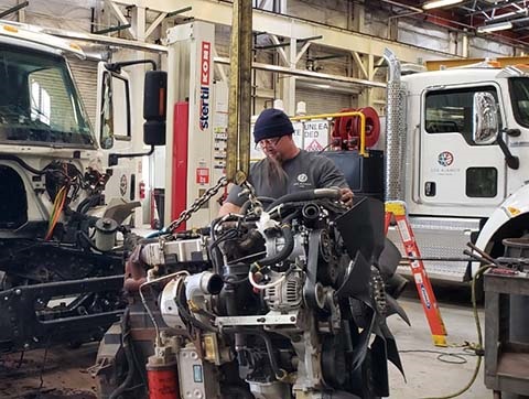 Photograph of the County's Fleet employee working on the engine of a county truck. He is wearing glasses, a beanie and a gray t-shirt branded with the county logo