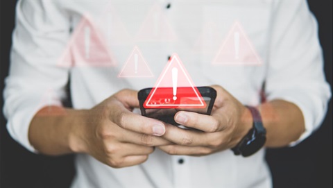 Image of a mad holding a cell phone with red triangle alert sign watermarks floating around it