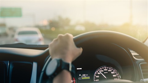 Safe Driving Stock Photo showing a hand on the steering wheel with traffic and road signs in the background