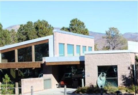 Two-story building with large windows surrounding by evergreen trees.
