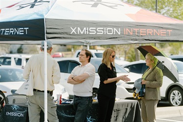 People standing under a tent with the words XMission Internet on it.