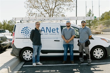 Three men stand in front of a vehicle that has LANet on the side.