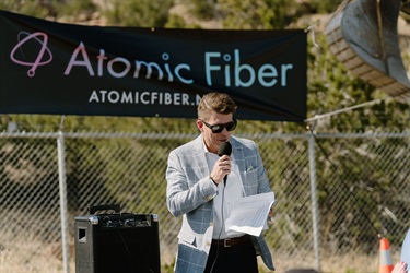 A man talking into a microphone with the banner that reads Atomic Fiber in the background