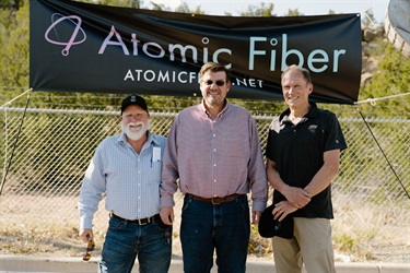 Three men stand in front of the banner that reads Atomic Fiber.