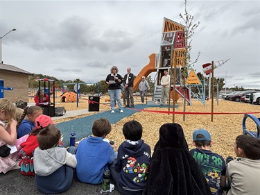 A woman speaks to a group of kids outdoors.