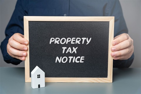 Image of a man holding a chalk board that says Property Tax Notice on it with a little wooden house sitting in front