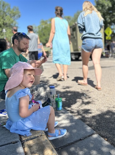A family sits on the curb waiting for the County Fair parade to begin.