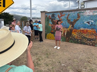 A woman standing and talks into a microphone in front of a large mosaic wall.