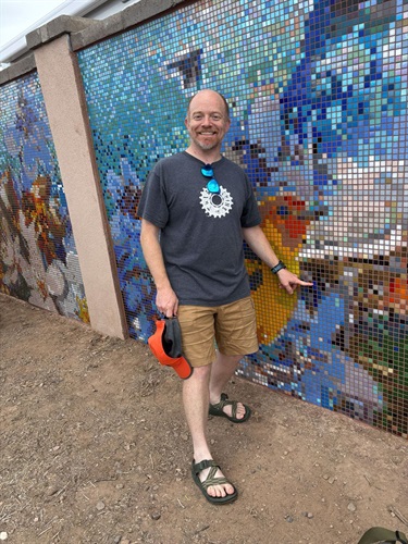 A man points near a bird depicted in a mosaic wall.