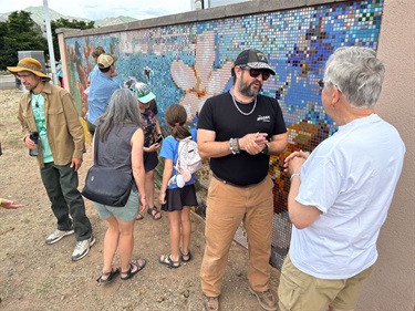 People talking and looking at a large mosaic wall.