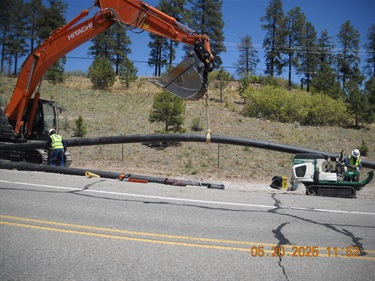 excavator lowering water pipe into trench