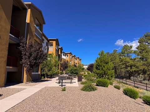 Multistory apartment complex with outdoor seating along a tree-lined multi-use path.