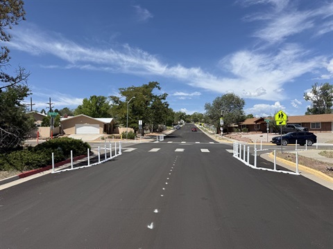View of a four-way road intersection with plastic bumpers and poles on either side to narrow the road width.