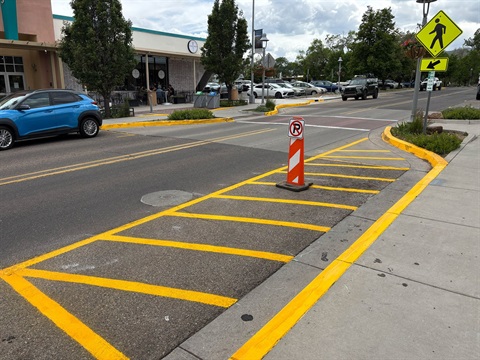 Yellow stripes on pavement show the closure of a parking space on the side of a two-lane road.