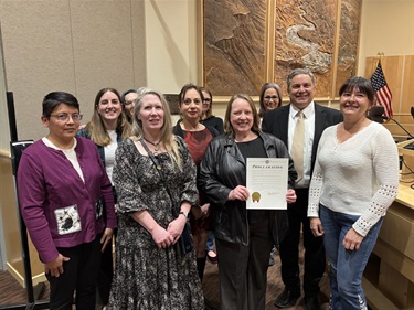A group of people stand together with one person in the middle holding a proclamation letter.