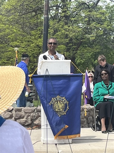 A woman speaks from behind a podium with a blue flag draped over it.