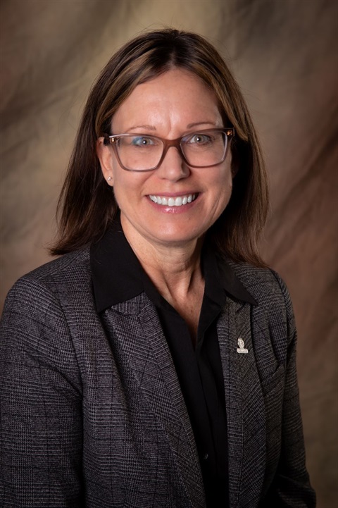 Portrait of County Manager Anne Laurent, smiling at the camera, wearing a gray suit with a black shirt.
