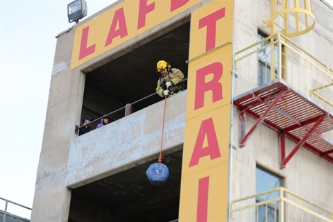Person leaning halfway out of a window pulls weight up the side of the LAFD Training Tower
